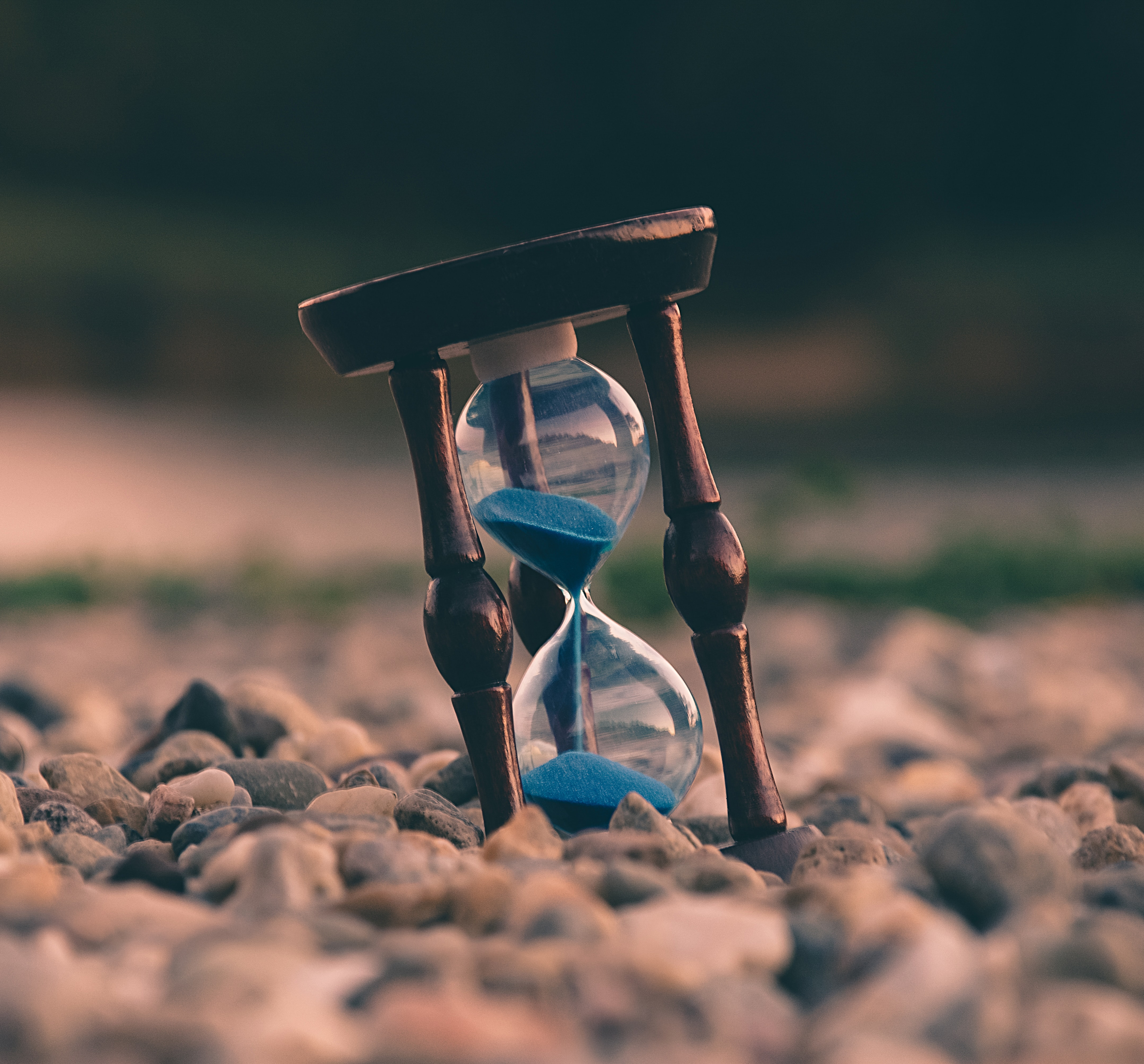 Wooden hourglass with blue sand sitting on a rocky beach